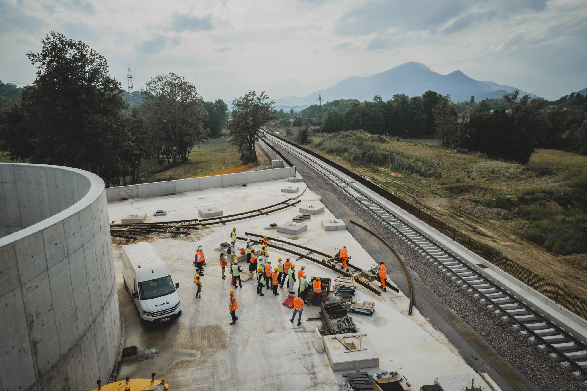 Aerial view of a Vossloh construction site with workers in safety vests next to newly laid tracks in a rural landscape
