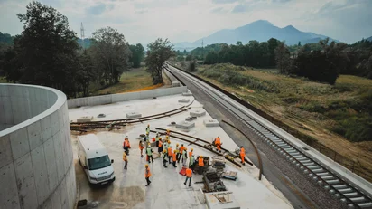 Aerial view of a Vossloh construction site with workers in safety vests next to newly laid tracks in a rural landscape